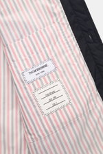 Innenseite der Thom Browne Daunenjacke navy mit kontrastfarbenem gestreiften Futter, Markenlabel und aufgesetzter Innentasche, Nahaufnahme.