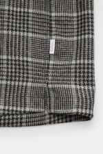 Nahaufnahme des unteren Saums mit kurzem Schlitz und kleinem Logo-Weblabel des 04651/ A trip in a bag Overshirt schwarz/grau kariert aus Woll-Mix mit Glencheck-Muster.
