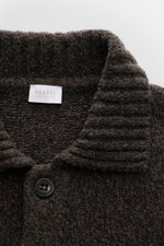 Close-up front view of the 04651/ A trip in a bag Cardigan 'Grainy' dunkelbraun, showing its ribbed collar, textured bouclé knit, and a dark button. Für moderne Layering-Looks: Der Cardigan 'Grainy' von 04651/ A TRIP IN A BAG wurde aus wärmendem Woll-Mix 