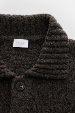 Close-up front view of the 04651/ A trip in a bag Cardigan 'Grainy' dunkelbraun, showing its ribbed collar, textured bouclé knit, and a dark button. Für moderne Layering-Looks: Der Cardigan 'Grainy' von 04651/ A TRIP IN A BAG wurde aus wärmendem Woll-Mix 
