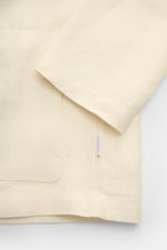 Detailaufnahme des cremefarbenen 04651/ A trip in a bag Overshirt 'Linen Jacket' aus weichem, reinem Leinen mit Slim Fit, Umlegekragen, Front- und Innentasche, fotografiert von schräg oben.