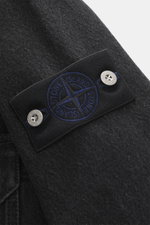 Close-up view of the compass badge on the upper arm of the Stone Island Denim Overshirt dark grey, showing denim made of pure cotton with typical material structure, slim fit, robust two-way zipper, turn-down collar, patch chest pocket, and buttoned sleev