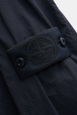 Nahaufnahme des Stone Island Overshirt 'Ghost Piece' navy Ärmels mit tonalem Kompass-Badge, Druckknopf und Microfaser-Textur, seitliche Perspektive.