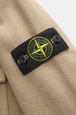 Close-up side view of the Stone Island Overshirt beige showing the typical compass badge on firm, felted virgin wool and microfiber fabric, featuring a patch chest pocket with flap. The garment is garment dyed with a slim fit, high-closing two-way zipper,