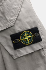 Nahaufnahme des Stone Island Overshirt 'Canvas' grau von oben rechts mit Fokus auf Canvas aus reiner Bio-Baumwolle, Kompass-Badge und aufgesetzter Tasche.