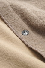 Nahaufnahme des Stone Island Overshirt beige aus Bouclé, Detail der leicht griffigen Woll-Microfaser mit Metall-Knopf, Perspektive von oben.