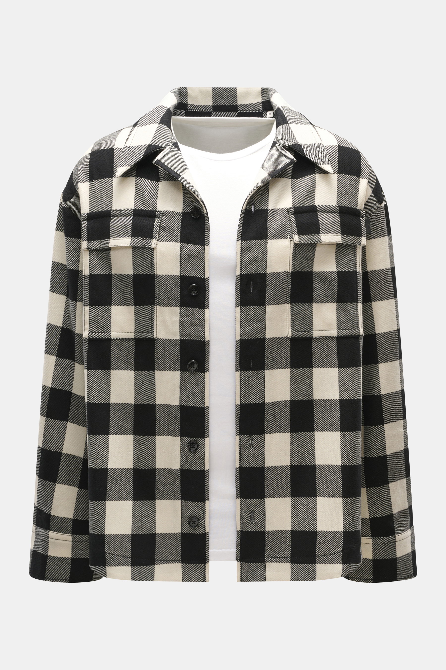 Ami Paris Overshirt black/cream checkered shown from the front, oversized fit, pure new wool lumberjack style with snap buttons, adjustable collar, patch chest pockets with flaps, classic sport cuffs, rounded hemline extended at the back, worn over a whit