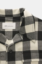 Close-up front view of the Ami Paris Overshirt black/cream checkered collar and chest pocket, made of pure wool with snap buttons.

Description: 
<p>Casual through the transitional season: The overshirt by AMI PARIS impresses with a loose fit made of pure