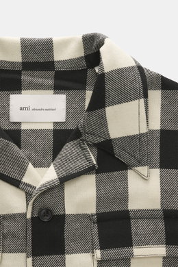Close-up front view of the Ami Paris Overshirt black/cream checkered collar and chest pocket, made of pure wool with snap buttons.

Description: 
<p>Casual through the transitional season: The overshirt by AMI PARIS impresses with a loose fit made of pure
