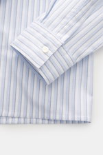 Close-up front view of Jacquemus Light blue/white striped overshirt cuff, oxford made of pure cotton, slightly textured feel, oversized fit, turn-down collar, two-way zipper, decorative J-hook, classic sport cuff, subtle logo stitching.