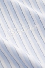 Close-up front view of Jacquemus Light blue/white striped overshirt showing pure cotton oxford fabric with a slightly textured feel, subtle logo stitching, and classic sport cuff details. Oversized fit with turn-down collar, two-way zipper, and decorative