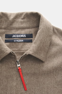 Close-up front view of Jacquemus Overshirt taupe meliert showing Umlegekragen, two-way zipper with decorative leather zipper pull, logo stitching on front, made of reine Schurwolle with weicher Griff, oversized fit, klassische Sportmanschette, and gerader