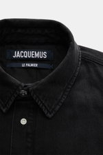 Nahaufnahme des schwarzen Jacquemus Overshirts aus Denim, reine Baumwolle, weicher Griff, Oversized Fit, Umlegekragen, glatte Knopfleiste, paspelierte Fronttaschen, Brusttasche mit Logo-Print, dekorativer J-Haken, klassische Sportmanschette, gerundeter Sa