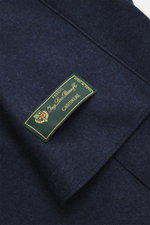 Close-up view of Harris Wharf London Cashmere overshirt navy melange fabric tag on pure cashmere, knitted and felted quality, very soft touch, raw-edge finish, slim fit, five-button placket, turn-down collar, patch chest pockets with flap, angled welt poc