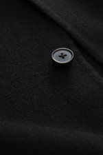 Nahaufnahme des schwarzen Officine Générale Overshirt 'Simao' mit Fokus auf Knopf, reine Wolle, weicher Griff, Regular Fit, Fünf-Knopf-Leiste, Stehkragen, aufgesetzte Fronttaschen, Unconstructed-Design, frontale Perspektive.