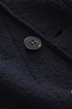 Nahaufnahme des Knopfes und Bouclé-Stricks aus reiner Schurwolle des 04651/ A trip in a bag Woll-Overshirt 'Boiled' navy, gewalkte Qualität, weicher Griff, Raw-Edge-Finish.