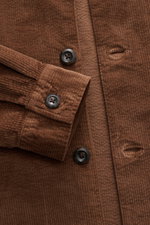 Nahaufnahme des braunen 04651/ A trip in a bag Cord-Overshirt Slim Fit aus Baumwoll-Cord mit Umlegekragen, Fünf-Knopf-Leiste, Taschen in der Seitennaht, klassischer Sportmanschette, leicht elastischer Qualität und softem Griff, fotografiert von oben.