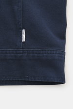 Nahaufnahme der dunkelblauen Baumwollstruktur mit Label an Saum, fotografiert aus seitlicher Perspektive des 04651/ A trip in a bag Overshirt 'Workwear Jacket' navy, reine Baumwolle, leicht griffige Haptik, Slim Fit, Fünf-Knopf-Leiste, Umlegekragen, aufge
