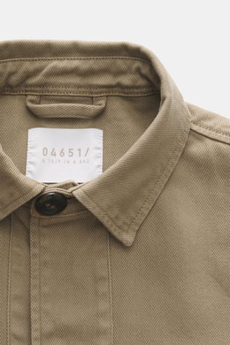Nahaufnahme des Kragens und Etiketts von 04651/ A trip in a bag Overshirt 'Workwear Jacket' taupe, reine Baumwolle, Slim Fit, Unconstructed Design, Fünf-Knopf-Leiste, Umlegekragen, leicht griffige Haptik, fotografiert aus frontaler Perspektive.