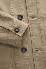 Nahaufnahme von 04651/ A trip in a bag Overshirt 'Workwear Jacket' taupe aus reiner Baumwolle, Slim Fit, Fünf-Knopf-Leiste, Umlegekragen, aufgesetzte Brusttaschen, Unconstructed Design, leicht griffige Haptik, von oben fotografiert.