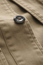 Nahaufnahme des Knopfes und Stoffdetails des Overshirts 04651/ A trip in a bag Overshirt 'Workwear Jacket' taupe, Slim Fit, reine Baumwolle, leicht griffig, Unconstructed Design, Fünf-Knopf-Leiste, Umlegekragen, aufgesetzte Brusttaschen, aus frontaler Per