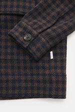 Nahaufnahme aus schräger Perspektive des Ärmels mit Manschette und Knopf sowie eines Teils der aufgesetzten Fronttasche des 04651/ A trip in a bag Overshirt 'Workwear Jacket' navy/braun kariert mit Karo-Webmuster, weichem Griff, Regular Fit, sechs-Knopf-L