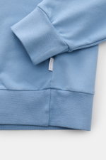 Nahaufnahme des Ärmel- und Saumbereichs vom 04651/ A trip in a bag Kapuzenpullover 'IF Hoodie' rauchblau aus weichem, gebürstetem Jersey mit Rippbündchen und kleinem Weblabel, fotografiert von oben.