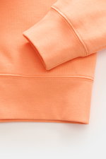 Nahaufnahme des hellorangefarbenen Polo Ralph Lauren Kapuzenpullovers, Fokus auf weiches Rippbündchen und Baumwoll-Microfaser-Mix.