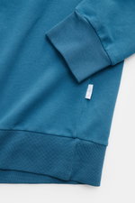 Nahaufnahme des petrolfarbenen 04651/ A trip in a bag Kapuzenpullover 'IF Hoodie' mit weichem, elastischem Jersey, Rippbündchen und kleinem Weblabel in Seitennaht.