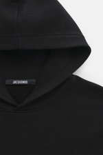 Jacquemus Kapuzenpullover 'Gros Grain' schwarz in Nahaufnahme von oben, Sweat aus reiner Baumwolle, schwere Qualität, softe Innenseite, markante Overlock-Nähte, Regular Fit, praktische Kapuze, Grosgrain mit Logo-Stitching auf der Brust, komfortable Rippbü
