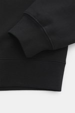 Nahaufnahme des Ärmelbündchens und Saums des Jacquemus Kapuzenpullover 'Gros Grain' schwarz, Sweat aus reiner Baumwolle, schwere Qualität, softe Innenseite, markante Overlock-Nähte, Regular Fit, praktische Kapuze, Grosgrain mit Logo-Stitching auf der Brus