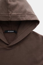 Nahaufnahme des Jacquemus Kapuzenpullover 'Gros Grain' graubraun von oben, Sweat aus reiner Baumwolle, schwere Qualität, softe Innenseite, markante Overlock-Nähte, Regular Fit, praktische Kapuze, Grosgrain mit Logo-Stitching, komfortable Rippbündchen.