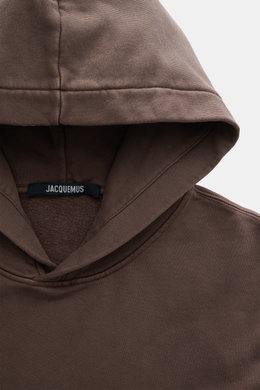 Nahaufnahme des Jacquemus Kapuzenpullover 'Gros Grain' graubraun von oben, Sweat aus reiner Baumwolle, schwere Qualität, softe Innenseite, markante Overlock-Nähte, Regular Fit, praktische Kapuze, Grosgrain mit Logo-Stitching, komfortable Rippbündchen.