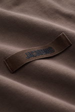 Nahaufnahme des Jacquemus Kapuzenpullover 'Gros Grain' graubraun, Sweat aus reiner Baumwolle, schwere Qualität, softe Innenseite, Regular Fit, praktische Kapuze, markante Overlock-Nähte, Grosgrain mit Logo-Stitching und komfortable Rippbündchen sichtbar.