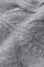 Nahaufnahme des von Braun Cashmere Rollkragenpullovers grau meliert, fotografiert aus schräger Perspektive, zeigt das klassische Zopfstrickmuster, weichen Griff und flexible Rippbündchen. Komfortabel durch die Winterzeit: Softer, zu einem klassischen Zopf