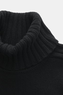 Nahaufnahme aus schräger Perspektive des Belstaff Rollkragenpullover 'Watch' schwarz mit grobem Strickbild, reiner Wolle, weichem Griff, Slim Fit, Rollkragen, Rippstrick-Elementen, flexible Rippbündchen und BELSTAFF-Weblabel auf der Brust.
