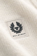 Nahaufnahme des grob gestrickten Belstaff Rollkragenpullovers 'Watch' creme, reine Wolle, weicher Griff, Slim Fit, Rollkragen, BELSTAFF-Weblabel auf der Brust, flexible Rippbündchen und Rippstrick-Elemente sichtbar.