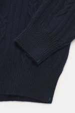 Close-up shot of Fioroni Cashmere turtleneck sweater navy, highlighting cable knit pattern, fine texture, and ribbed cuffs, viewed from above.