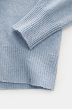 Close-up top-down view of B.F. Knitwear Cashmere Turtleneck Sweater light blue melange showing soft pure cashmere, medium-fine knit, slim fit, fitted turtleneck, and elastic rib-knit cuffs.