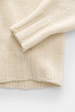 Close-up top view of B.F. Knitwear Cashmere turtleneck sweater cream showing coarse knit texture, fitted turtleneck, and elastic ribbed cuffs.