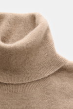 Nahaufnahme aus schräger Perspektive des Brunello Cucinelli Cashmere Rollkragenpullovers beige meliert mit feinem Strickbild und anliegendem Rollkragen.