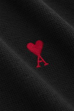 Close-up view of the Ami Paris Merino Turtle Neck Sweater Black showing fine knit pattern and red heart logo stitching on black merino wool fabric.