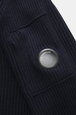 Close-up top view of the navy C.P. Company Turtleneck sweater showing medium-fine knit, rib stitch, lens detail, zippered upper arm pocket, and soft virgin wool microfiber.