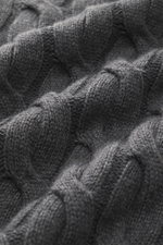 Nahaufnahme des Moorer Rollkragenpullover 'Gordon' dunkelgrau meliert aus Wolle-Cashmere-Mix mit grobem Zopfmuster, fotografiert aus schräger Perspektive.