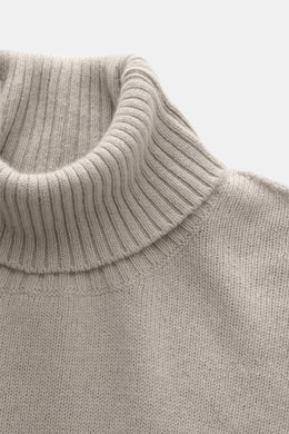 Nahaufnahme des anliegenden Rollkragens vom 04651/ A trip in a bag Cashmere Rollkragenpullover sand, mittelfeines Strickbild, reiner Cashmere, weicher Griff, Slim Fit mit komfortablen Rippbündchen, fotografiert aus seitlicher Perspektive.