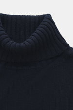Nahaufnahme aus leicht seitlicher Perspektive des von Braun Merino Rollkragenpullovers navy mit mittelfeinem Strickbild, Oversized Fit, Rippstrick-Rollkragen und flexiblen Rippbündchen aus reiner Merinowolle.