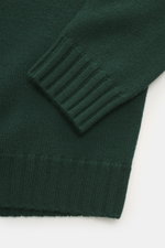 Nahaufnahme des von Braun Merino Rollkragenpullovers dunkelgrün, fotografiert schräg von oben, mittelfeines Strickbild, Rippstrick-Rollkragen und flexible Rippbündchen sichtbar.