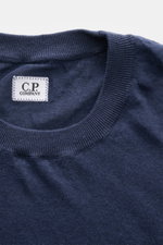 Nahaufnahme des C.P. Company Kurzarmpullovers navy aus feinstem Leinenstrick, weicher Griff, Regular Fit, elastische Rippbündchen und Weblabel am Saum, fotografiert von oben.