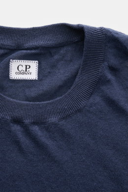 Nahaufnahme des C.P. Company Kurzarmpullovers navy aus feinstem Leinenstrick, weicher Griff, Regular Fit, elastische Rippbündchen und Weblabel am Saum, fotografiert von oben.