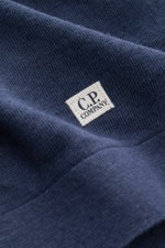Nahaufnahme des weichen Strickbilds und des kleinen Weblabels am Saum des C.P. Company Kurzarmpullover navy aus feinstem Leinen.